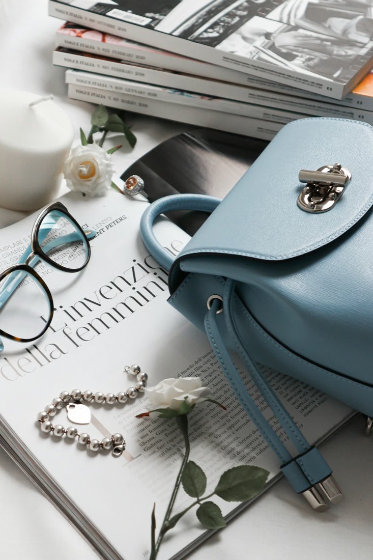 Bolsa de couro azul, óculos, revista e pulseira